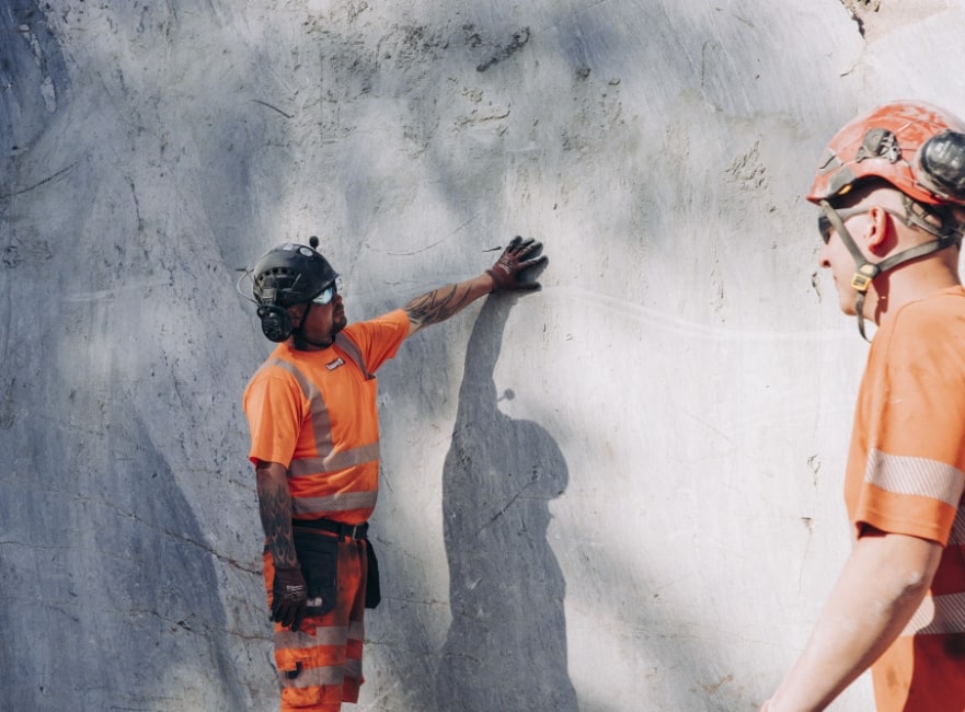 kaksi louhinnan työntekijää tarkastelevat kallioseinämää